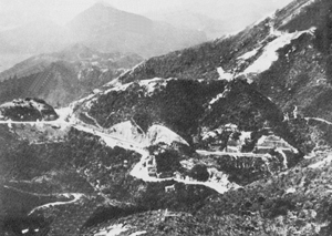 Le col de Wong-Nei-Chong, scène d'un des plus sanglants épisodes de la bataille de Hong Kong. C'est ici qu'une compagnie des <em>Winnipeg Grenadiers</em> défendit sa position pendant plusieurs jours, retardant les Japonais et leur infligeant de lourdes pertes. La  principale route nord-sud de l'île s'étend de droite à gauche sur toute la largeur de la photo. (<em>Musée canadien de la guerre J-2055312)</em>