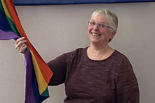 Patti Gray souriant en tenant un drapeau arc-en-ciel de la Fierté.